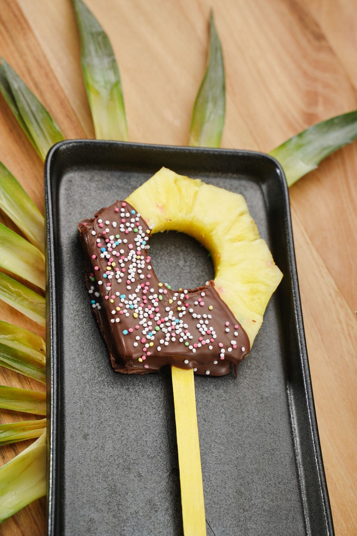 horizontal view of Chocolate Coated Pineapple Pop on a black tray
