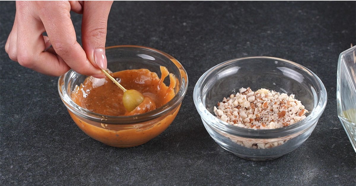grape on a toothpick being dipped into caramel sauce