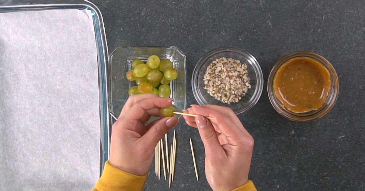 hands inserting a toothpick into a grape to make Caramel Apple Grapes