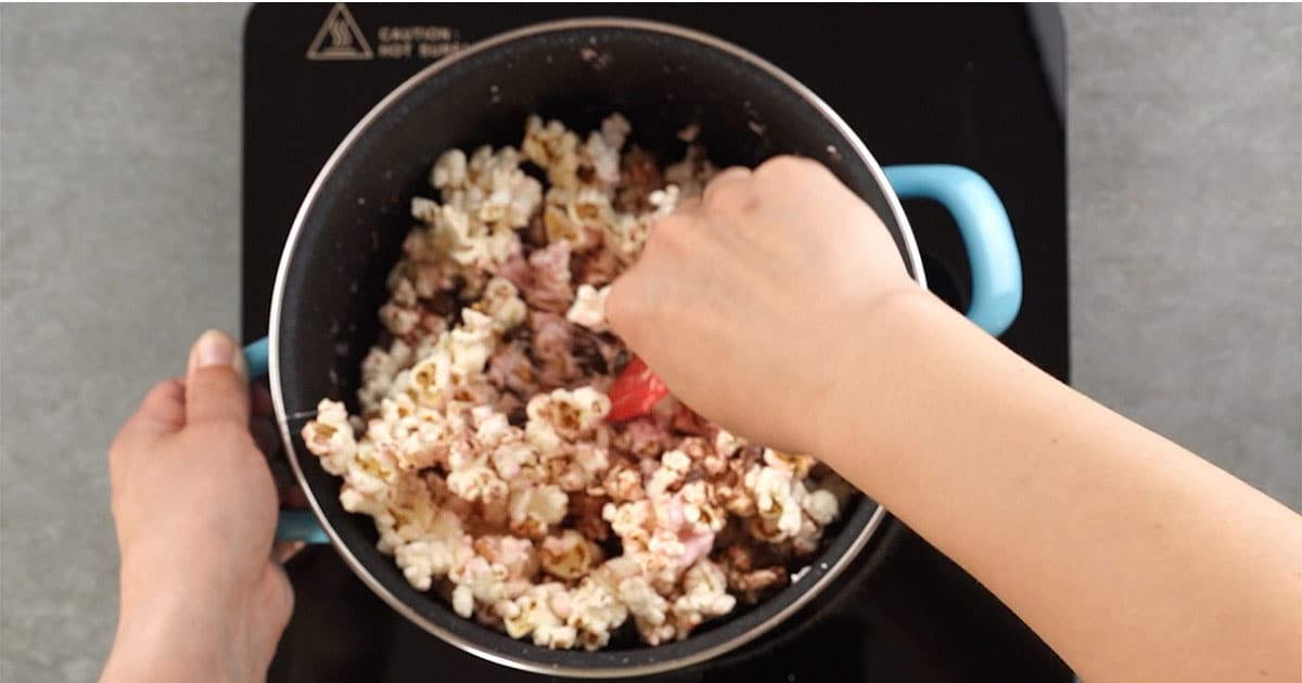 stirring a mixture of popcorn and chocolate to make rocky road popcorn balls