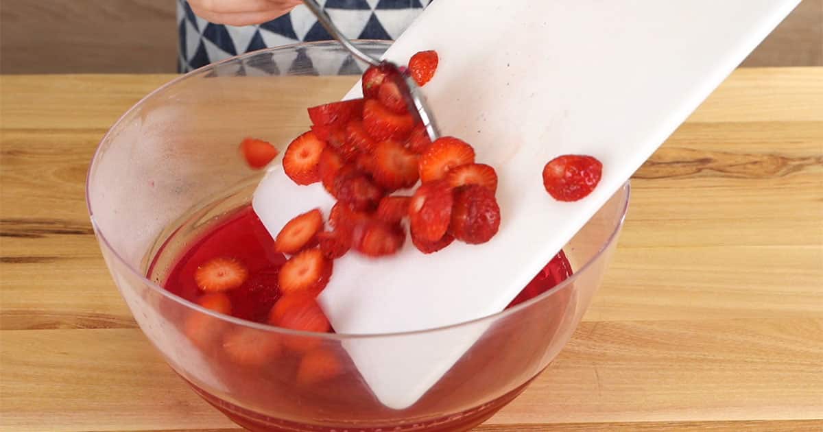 adding sliced strawberries to a bowl of strawberry jello to make strawberry champagne jello