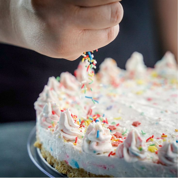 hand adding sprinkles to the top of a no-bake funfetti cheesecake