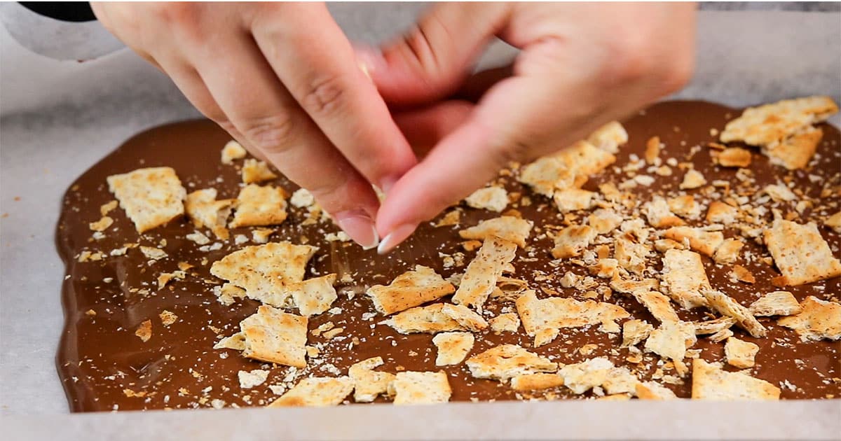 graham cracker crumbs being crumbled over melted chocolate