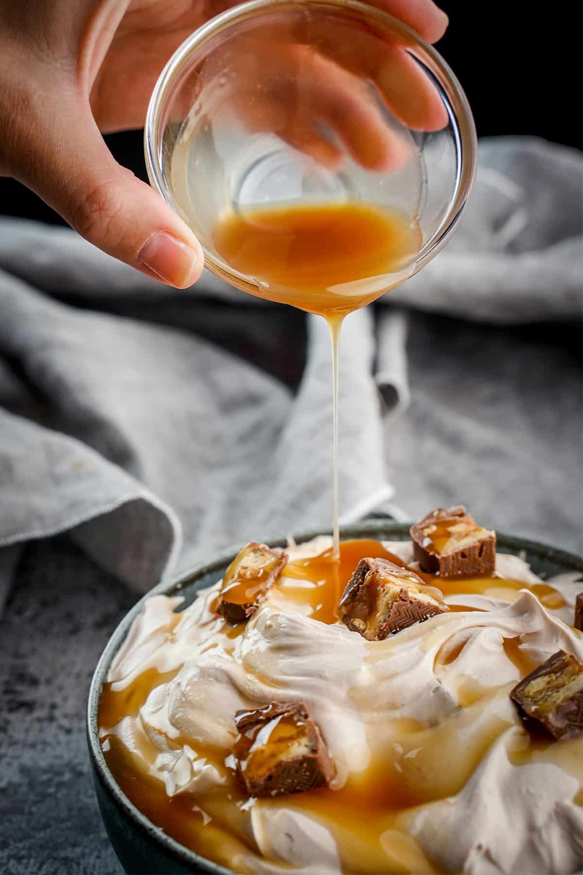 caramel being drizzled over a bowl of Snickers dip
