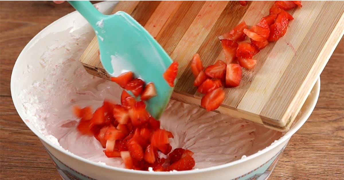 adding sliced strawberry to other ingredients to make strawberry cheesecake popsicles