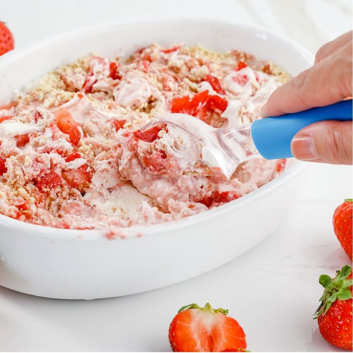 strawberry cheesecake ice cream being scooped out of a large bowl